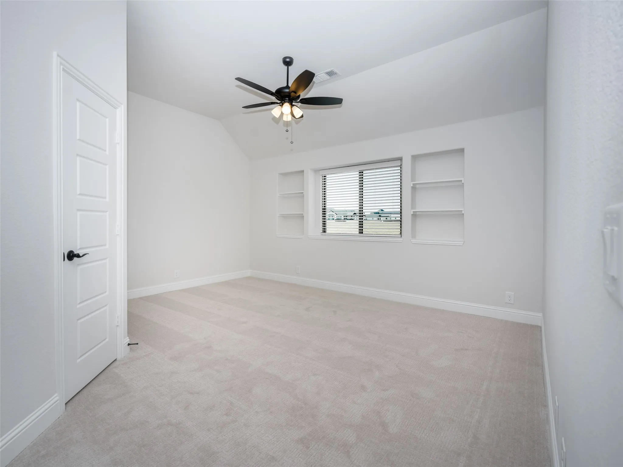 Spare room featuring light carpet, lofted ceiling, built in shelves, and ceiling fan