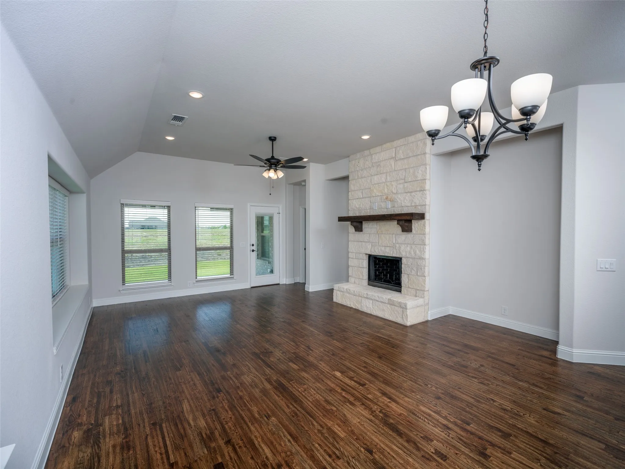 Unfurnished living room featuring a ceiling fan, dark wood finished floors, a fireplace, a chandelier, and vaulted ceiling