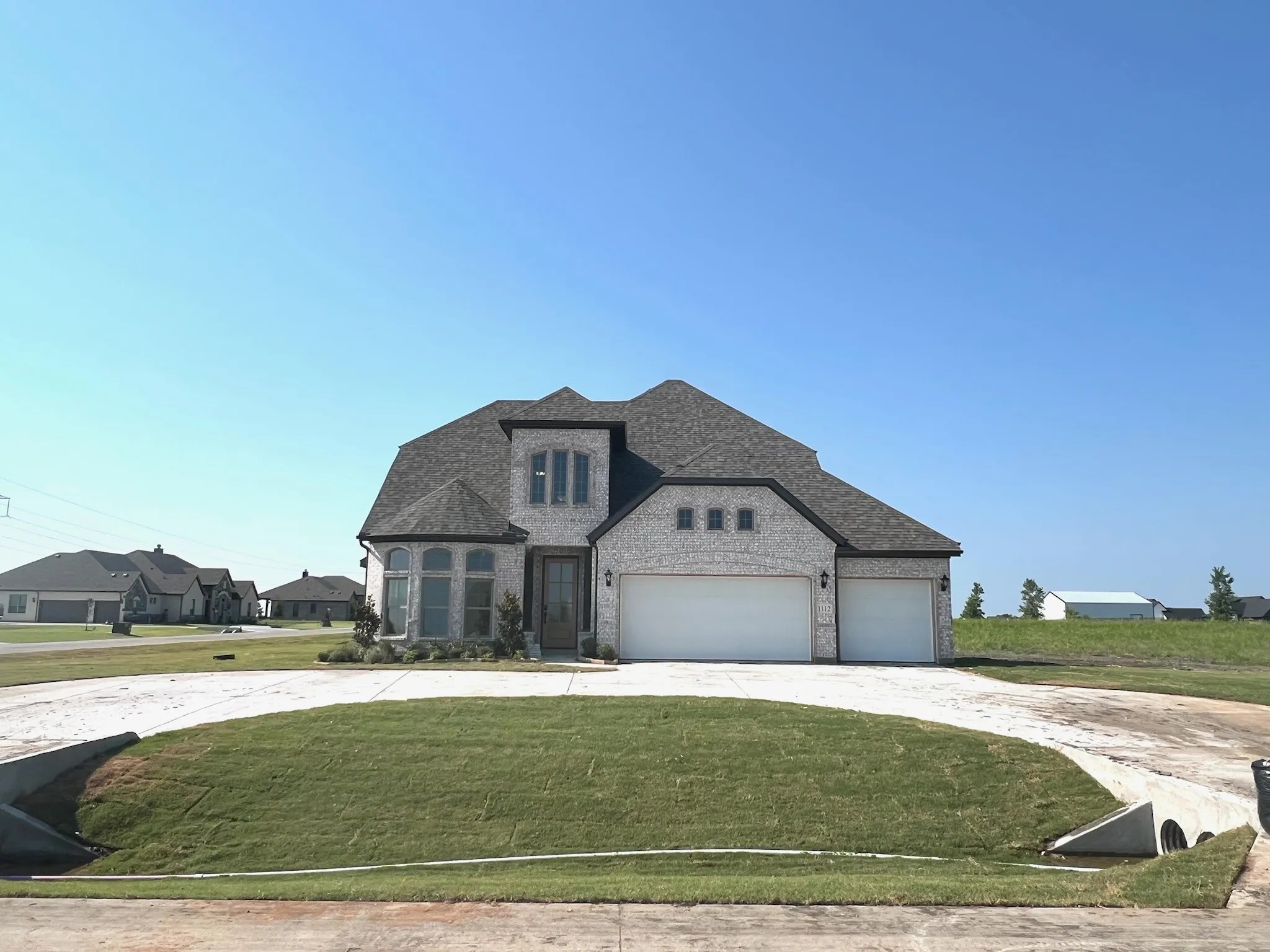 French provincial home featuring a front lawn, curved driveway, brick siding, and a shingled roof