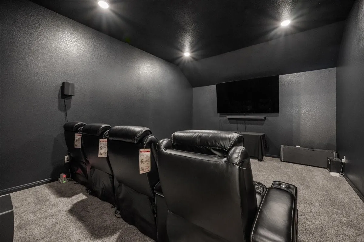 Home theater room featuring a textured wall, lofted ceiling, and carpet floors