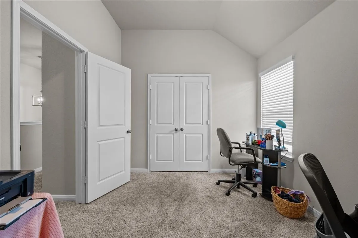 Carpeted home office featuring vaulted ceiling and baseboards