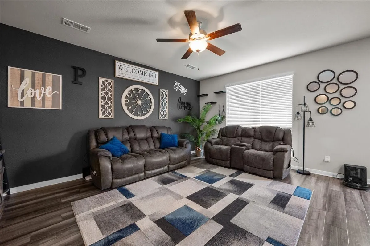 Living area with wood finished floors, a ceiling fan, and a wood stove