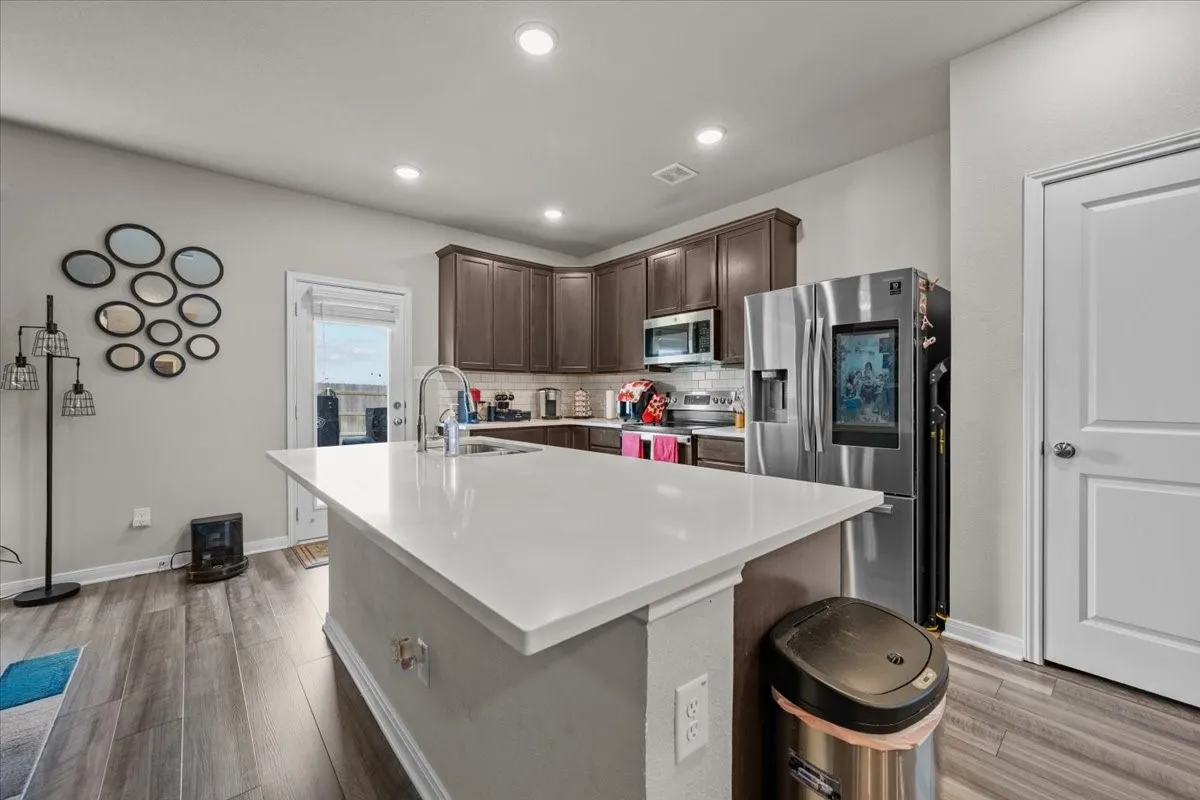 Kitchen with appliances with stainless steel finishes, decorative backsplash, light countertops, dark brown cabinets, and light wood finished floors