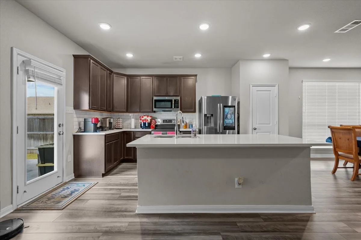 Kitchen with dark brown cabinets, appliances with stainless steel finishes, backsplash, light countertops, and an island with sink