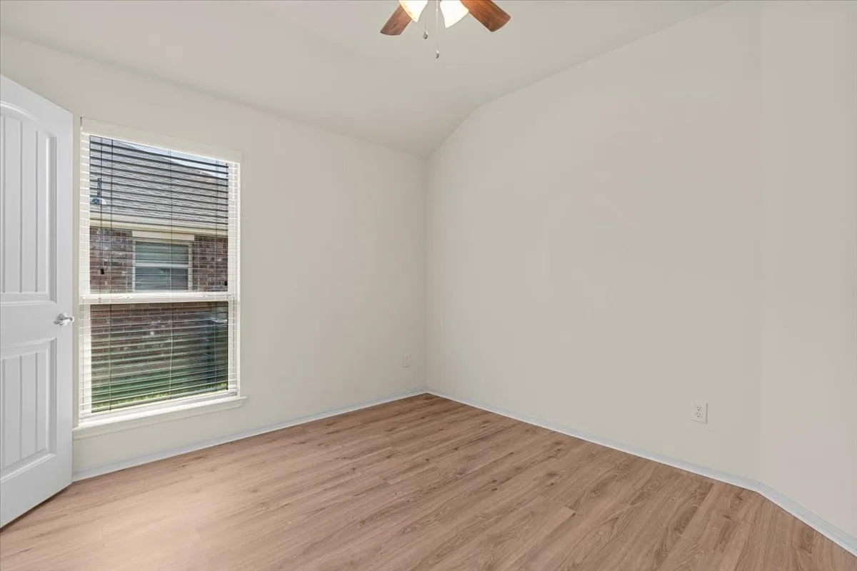 Spare room featuring light wood-type flooring, vaulted ceiling, and ceiling fan