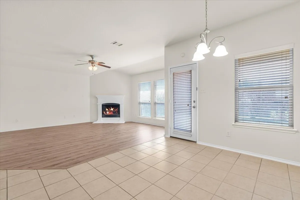 Unfurnished living room with light tile patterned flooring, a warm lit fireplace, a ceiling fan, and a chandelier