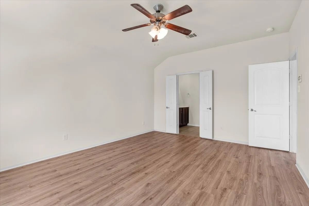 Unfurnished bedroom with light wood-style floors, lofted ceiling, ensuite bath, and ceiling fan