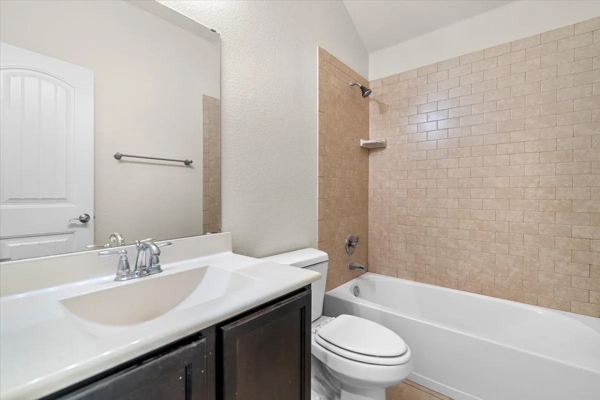 Bathroom with a textured wall, vanity, bathtub / shower combination, and vaulted ceiling