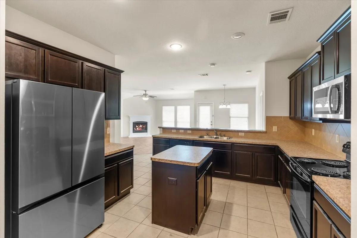 Kitchen with appliances with stainless steel finishes, light tile patterned floors, backsplash, dark brown cabinetry, and recessed lighting