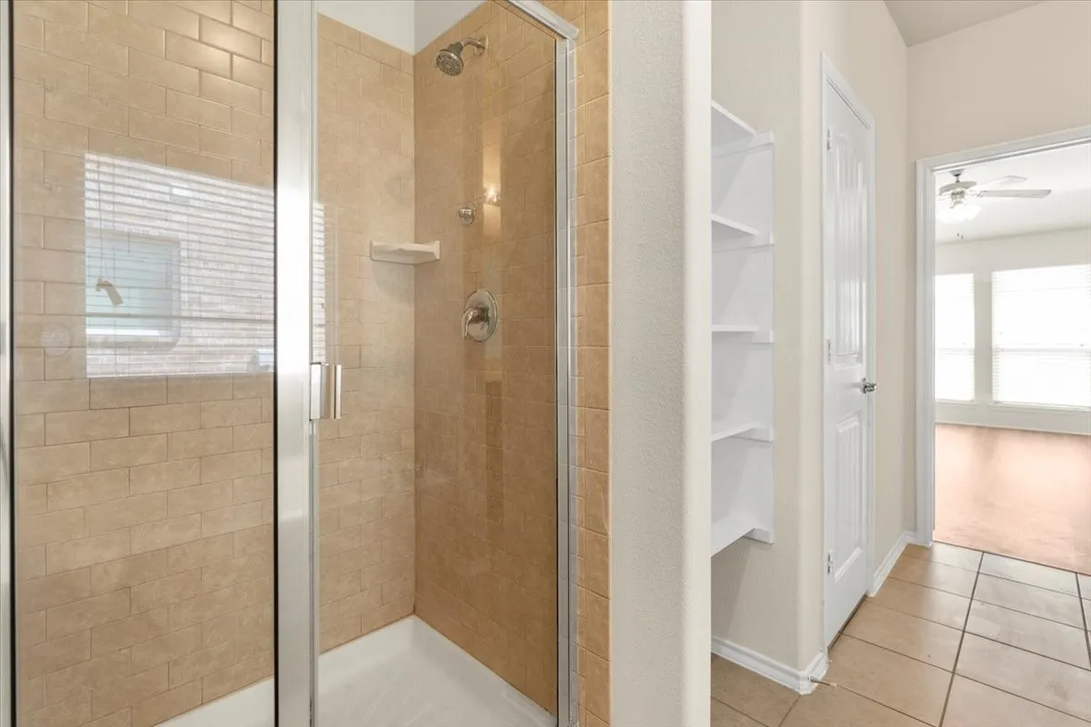 Bathroom with a stall shower, tile patterned floors, ceiling fan, and built in shelves