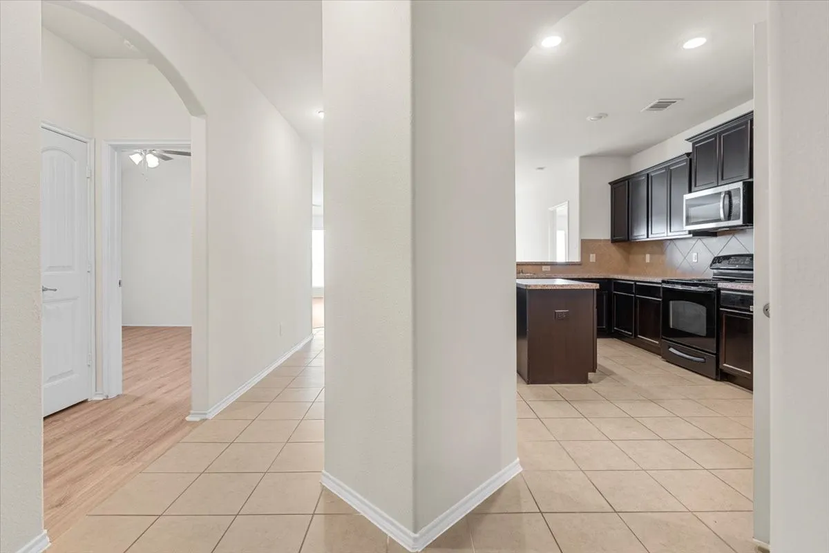 Kitchen featuring decorative backsplash, black range with electric cooktop, light tile patterned flooring, arched walkways, and stainless steel microwave