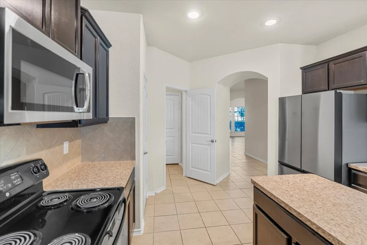 Kitchen featuring arched walkways, appliances with stainless steel finishes, dark brown cabinetry, tasteful backsplash, and light tile patterned floors