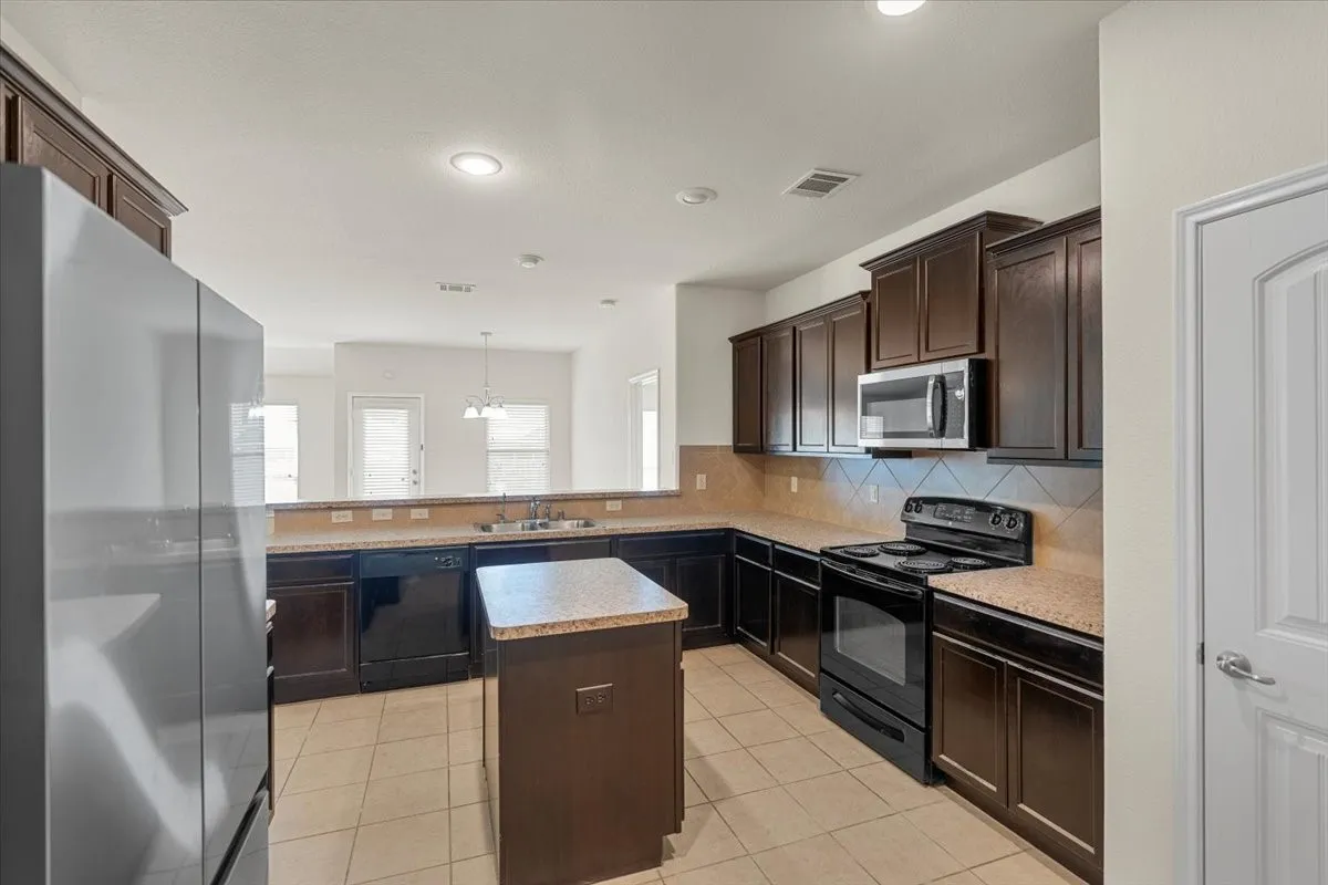 Kitchen featuring black appliances, backsplash, a center island, light tile patterned floors, and dark brown cabinetry