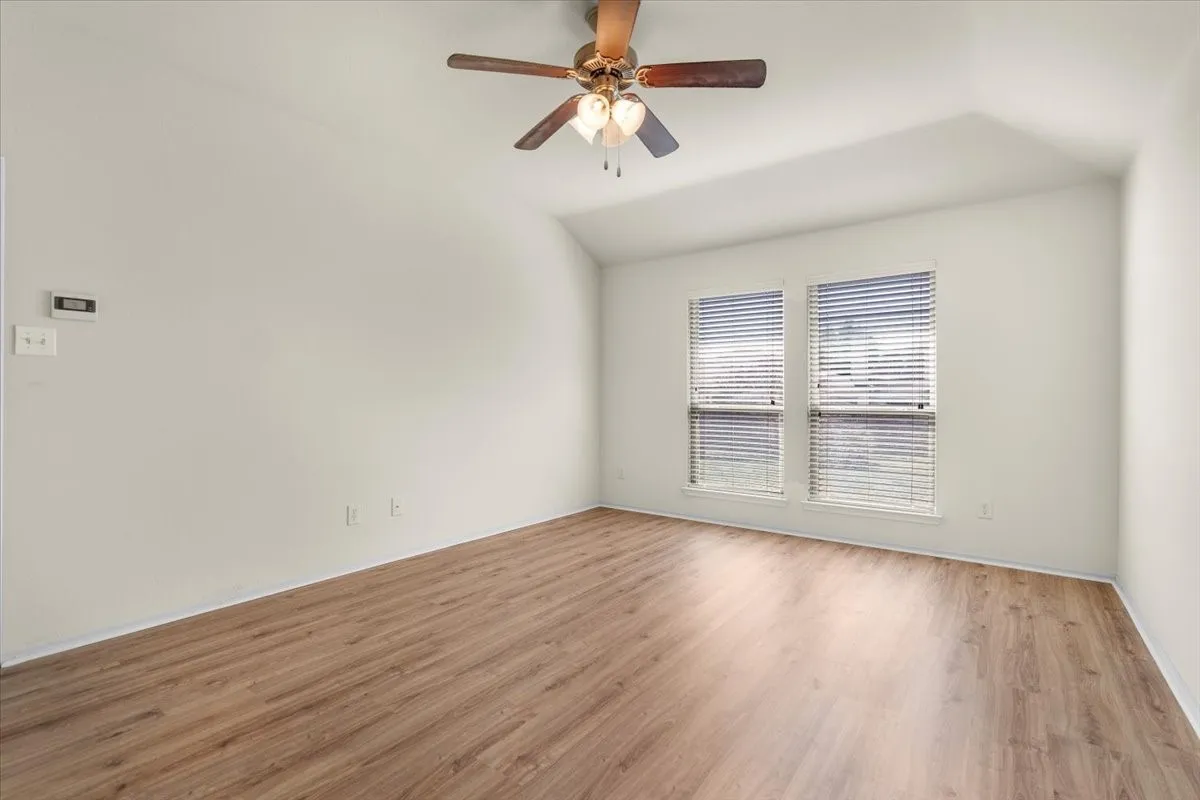 Empty room featuring light wood-style floors, vaulted ceiling, and ceiling fan