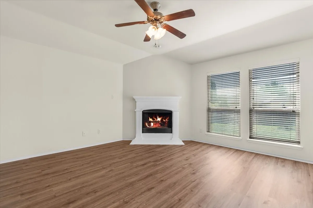 Unfurnished living room with wood finished floors, a lit fireplace, and a ceiling fan