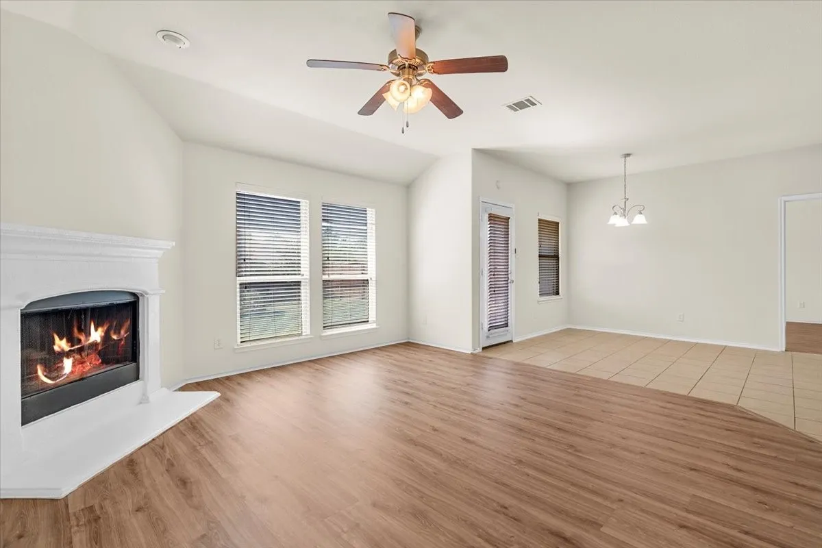Unfurnished living room with a warm lit fireplace, light wood finished floors, ceiling fan, a chandelier, and vaulted ceiling