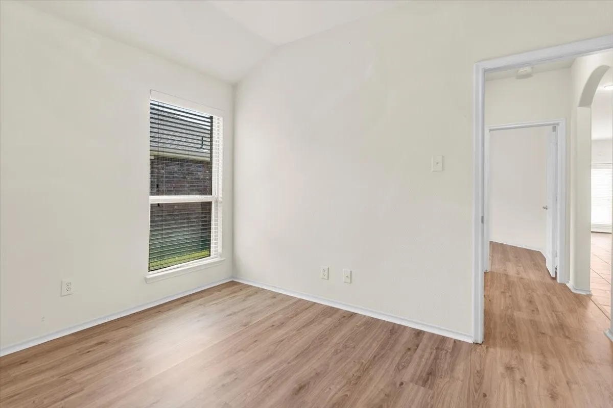 Spare room featuring light wood finished floors, arched walkways, and vaulted ceiling