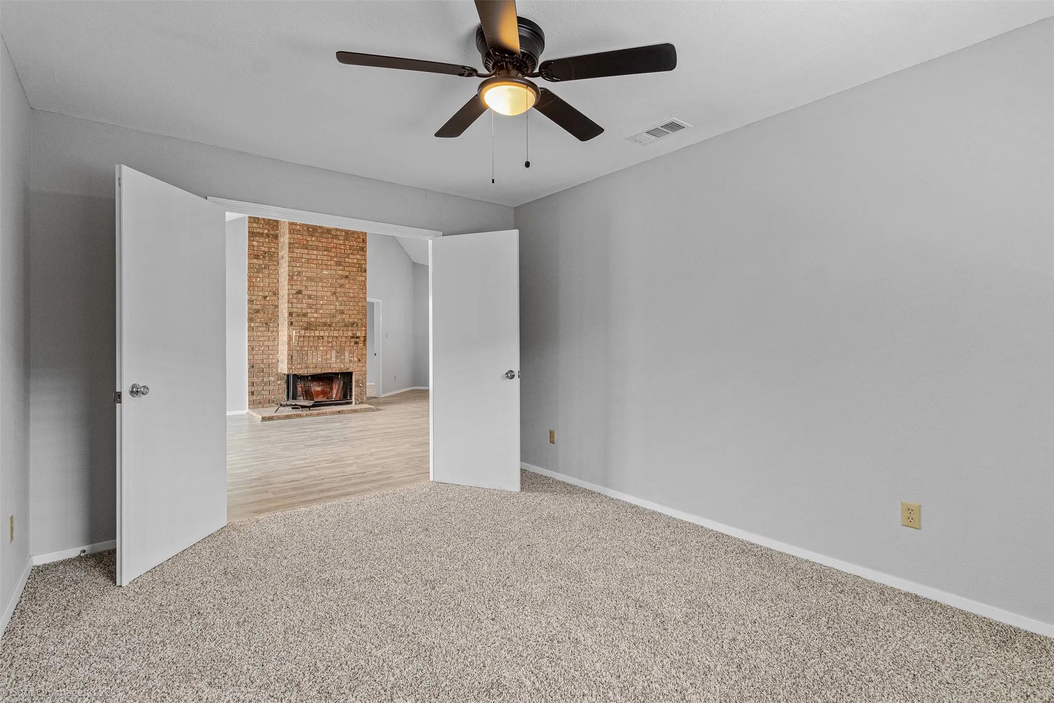 Carpeted empty room featuring a ceiling fan and a brick fireplace
