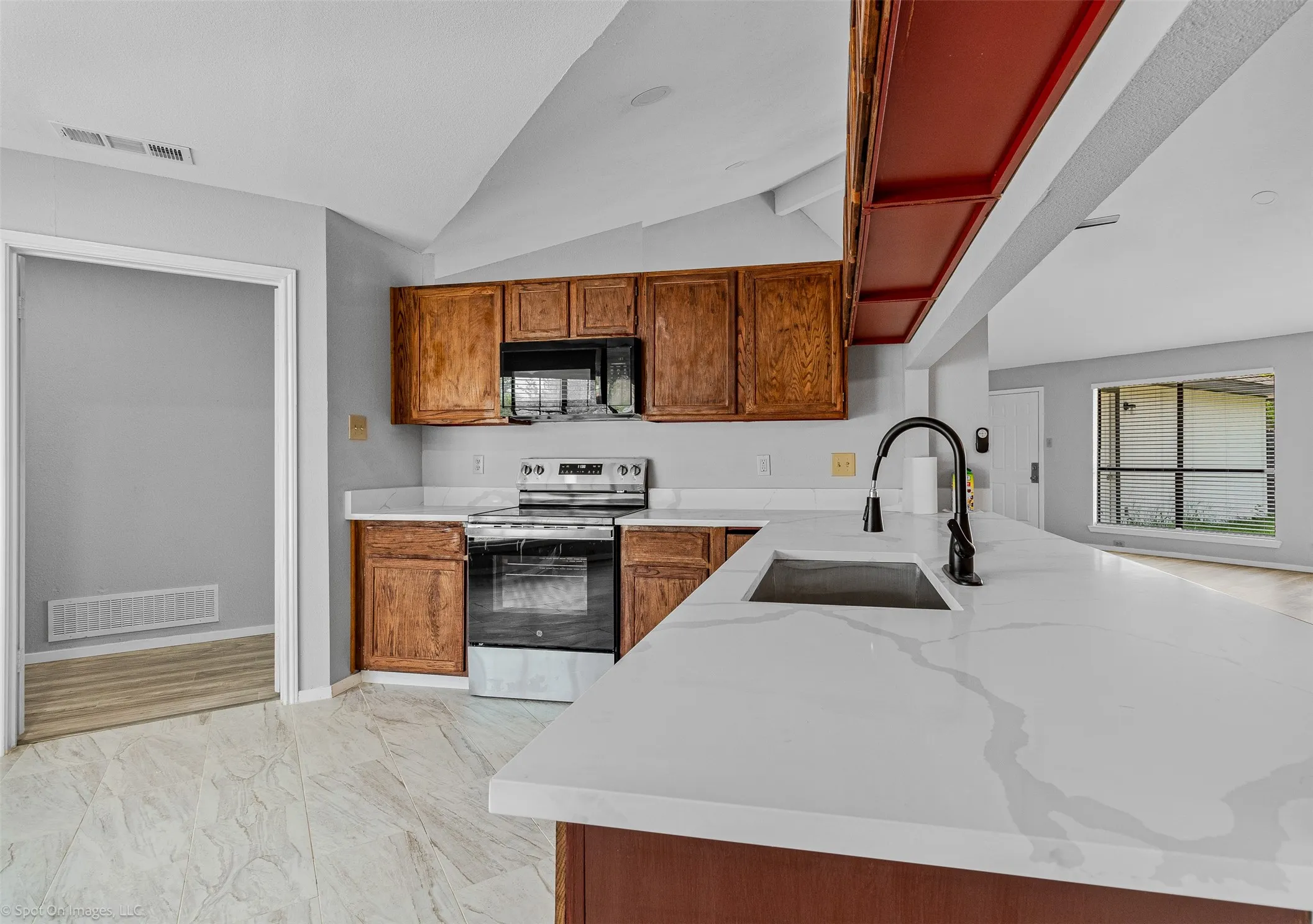 Kitchen featuring stainless steel range oven, lofted ceiling, brown cabinets, and light stone counters