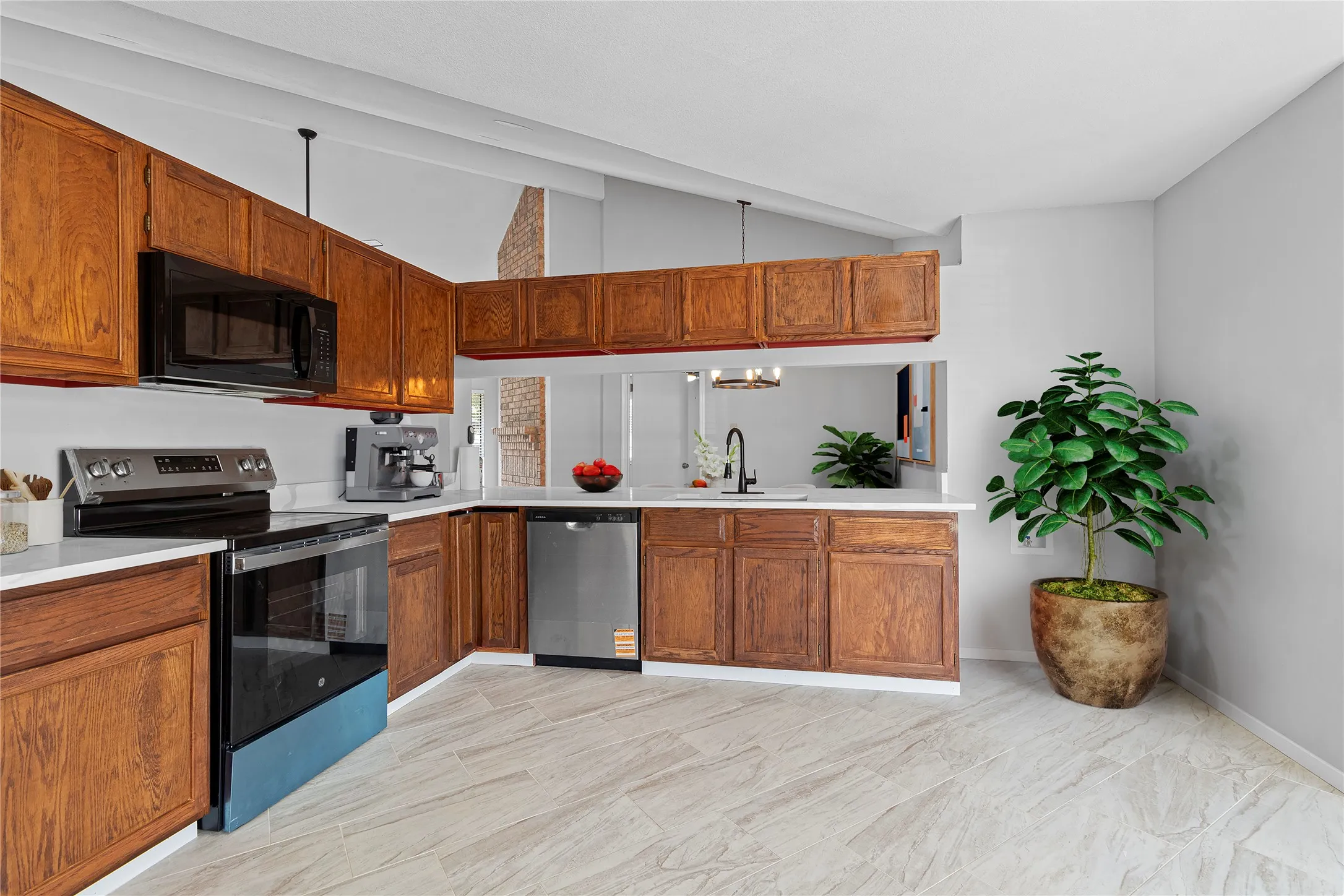 Kitchen featuring stainless steel appliances, light countertops, vaulted ceiling, and brown cabinetry