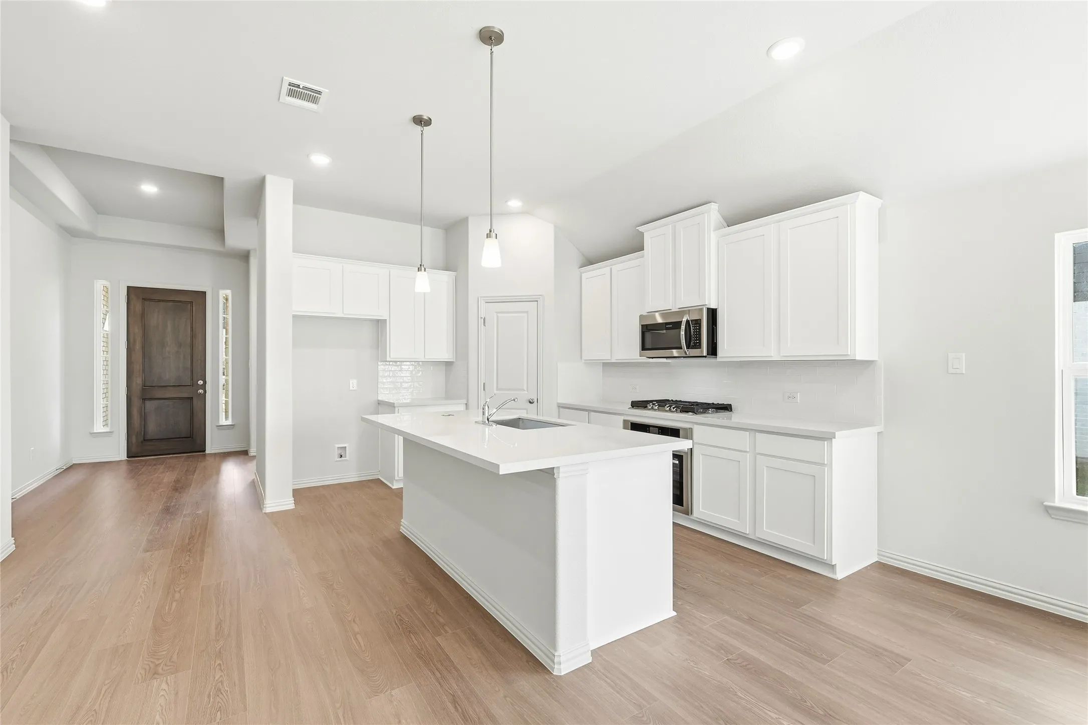 Kitchen with white cabinetry, light wood finished floors, hanging light fixtures, an island with sink, and stainless steel appliances