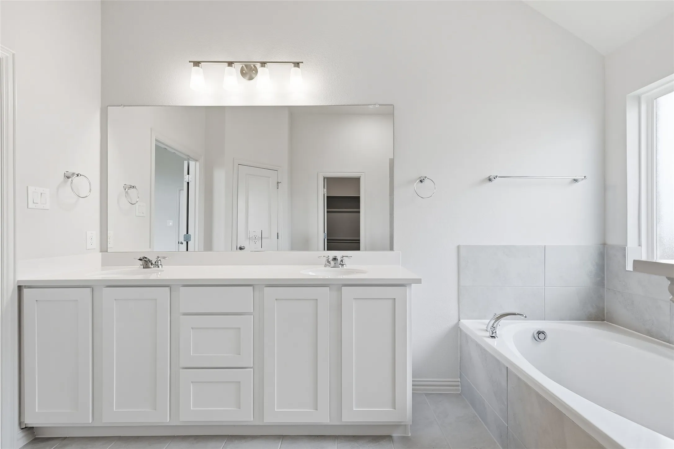 Bathroom featuring a bath, double vanity, lofted ceiling, and light tile patterned floors