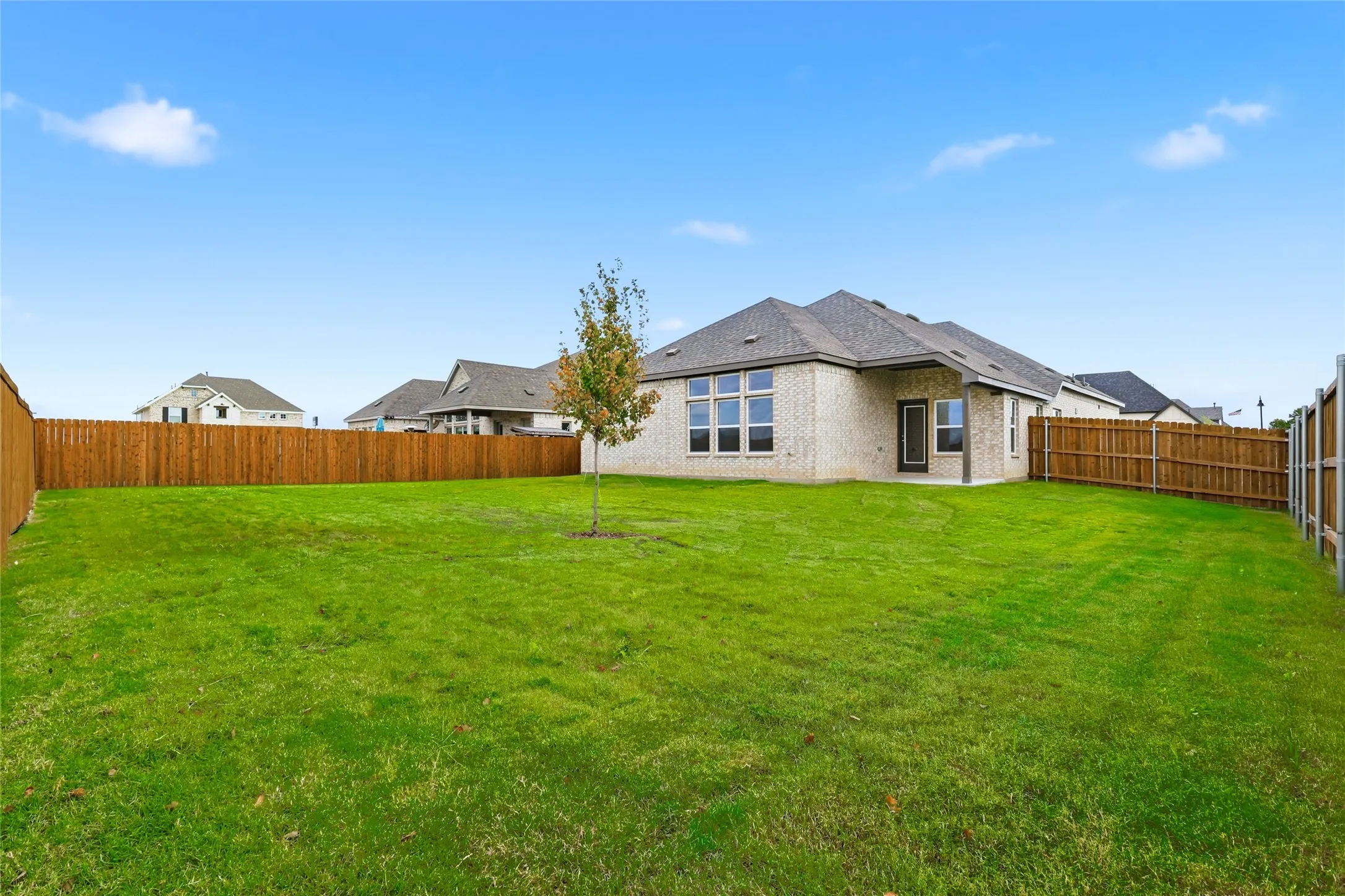 Back of property with brick siding, a fenced backyard, and a patio area