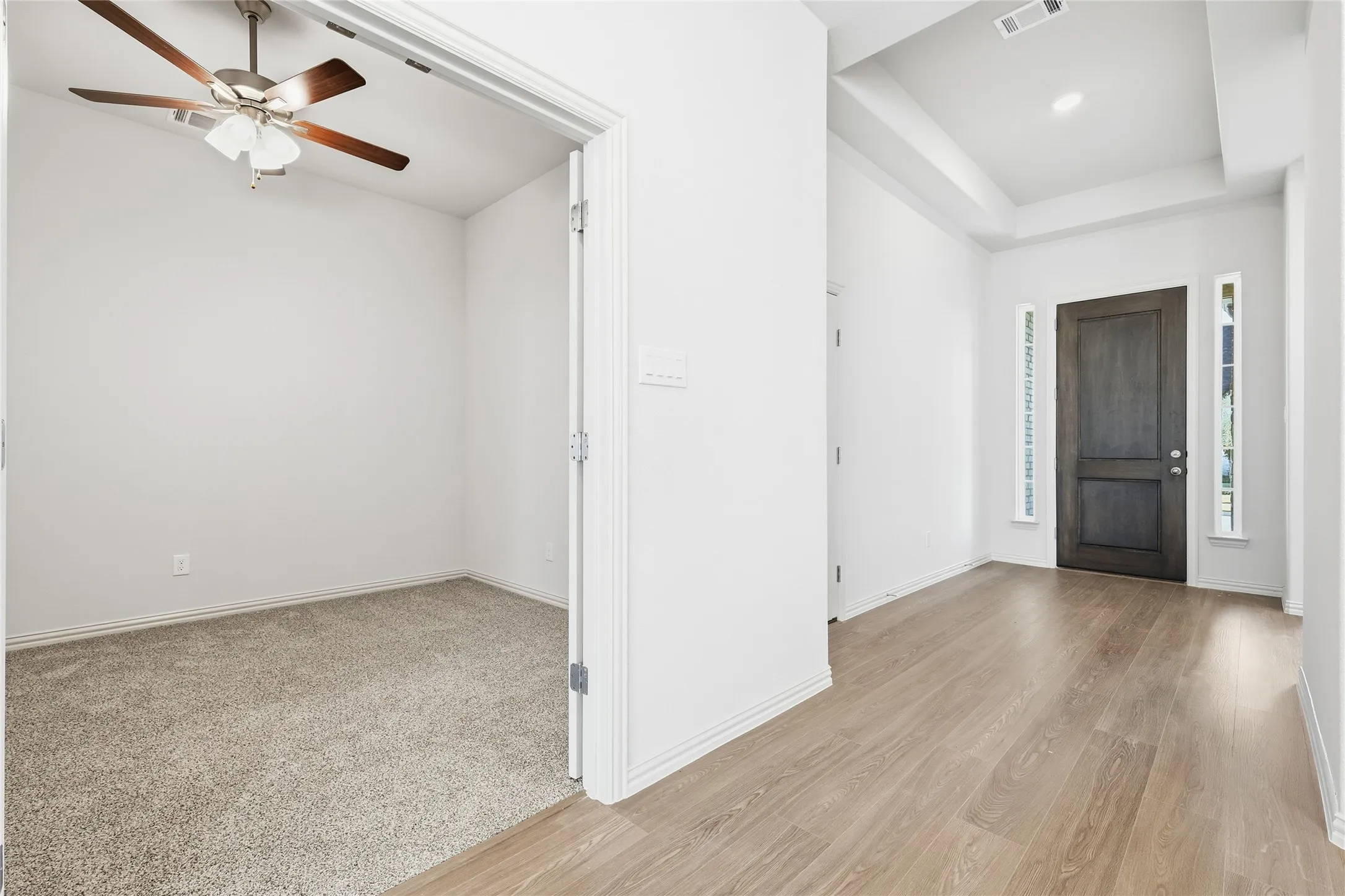 Entryway featuring ceiling fan, light wood-style flooring, a tray ceiling, and light colored carpet