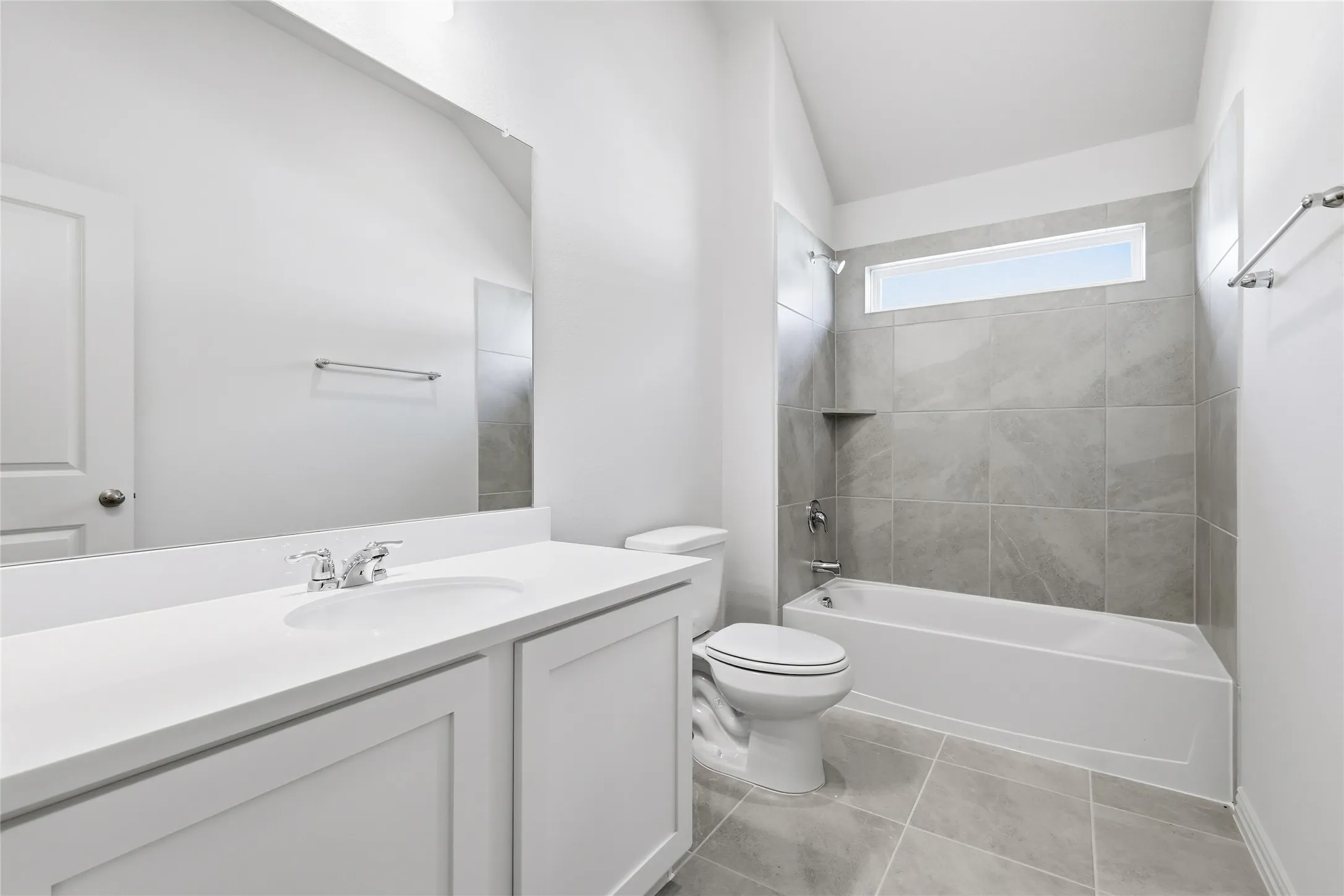 Bathroom featuring bathing tub / shower combination, vanity, light tile patterned floors, and vaulted ceiling