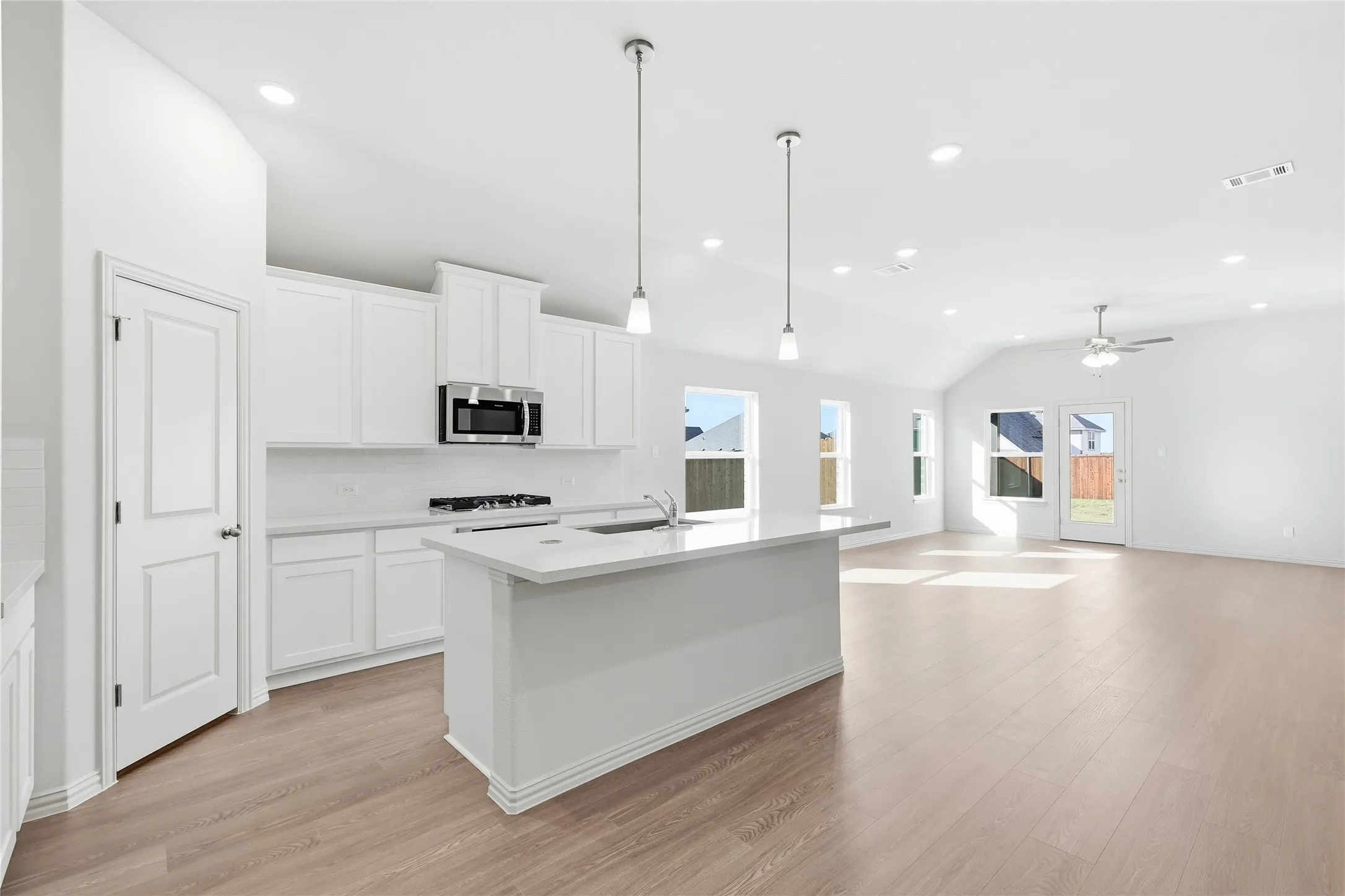 Kitchen featuring decorative light fixtures, vaulted ceiling, white cabinetry, a kitchen island with sink, and light wood-style flooring