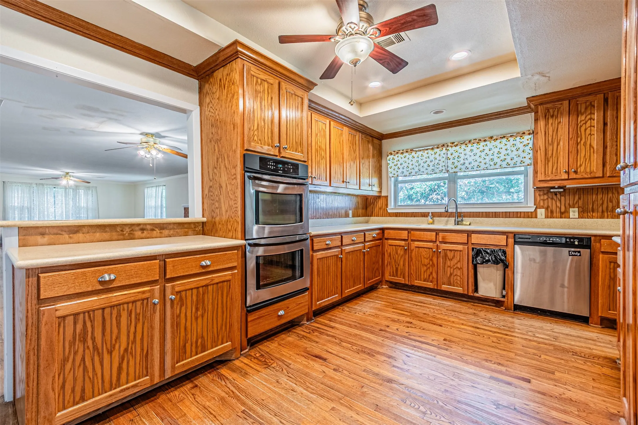 Kitchen featuring a ceiling fan, a tray ceiling, light countertops, stainless steel appliances, and light wood-style floors