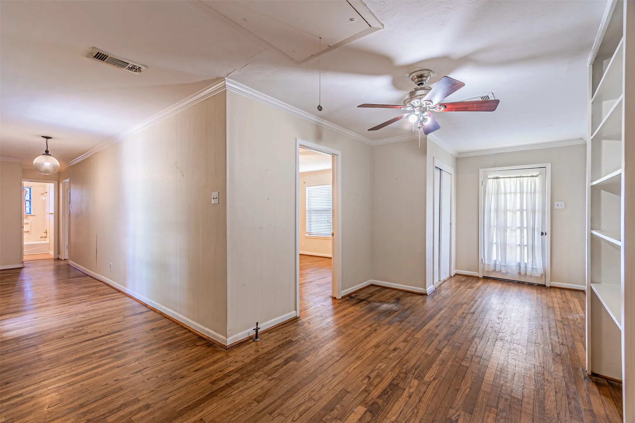 Unfurnished room with attic access, crown molding, dark wood-type flooring, and a ceiling fan