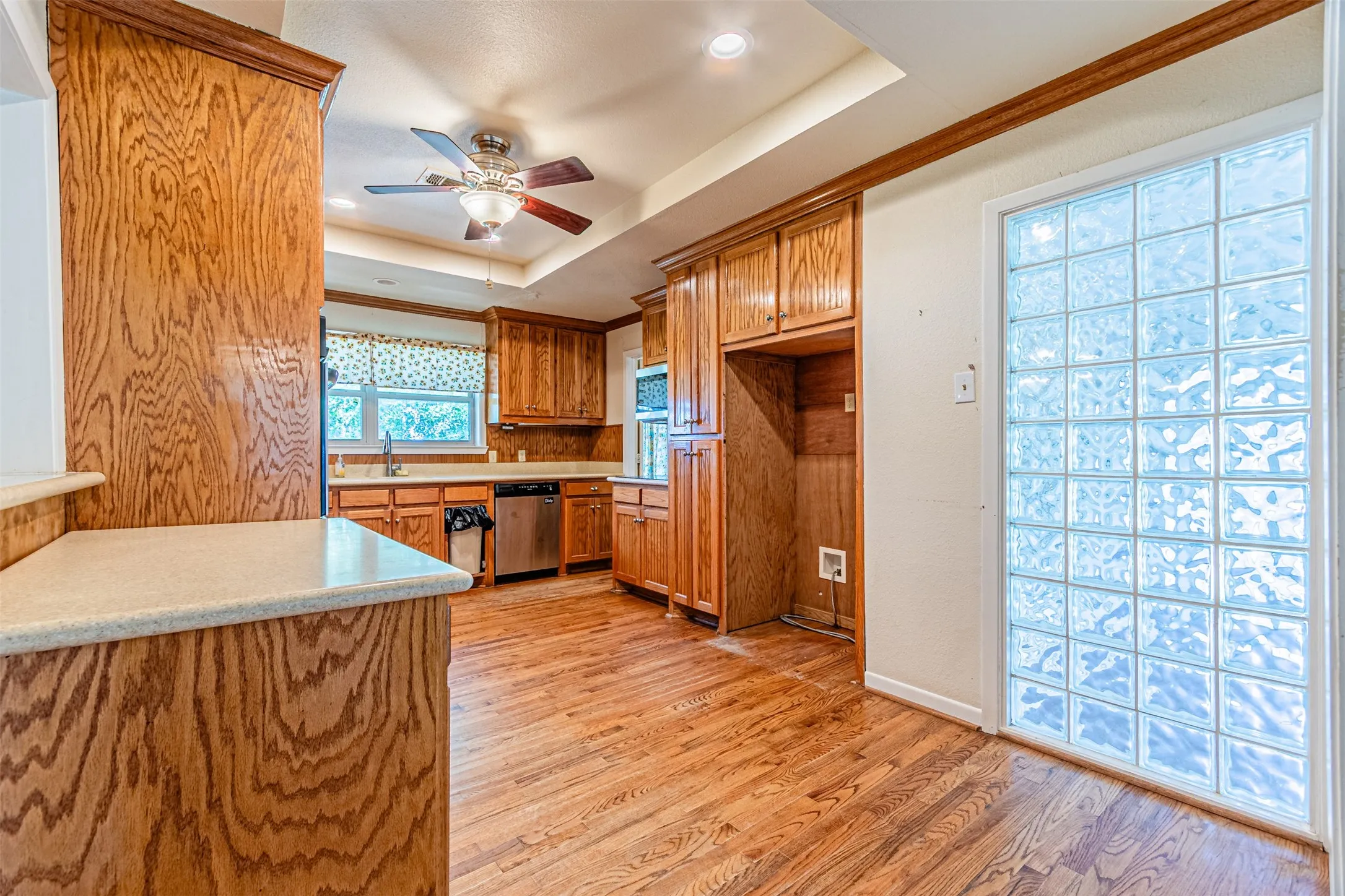 Kitchen featuring brown cabinets, a raised ceiling, light countertops, light wood-style floors, and recessed lighting