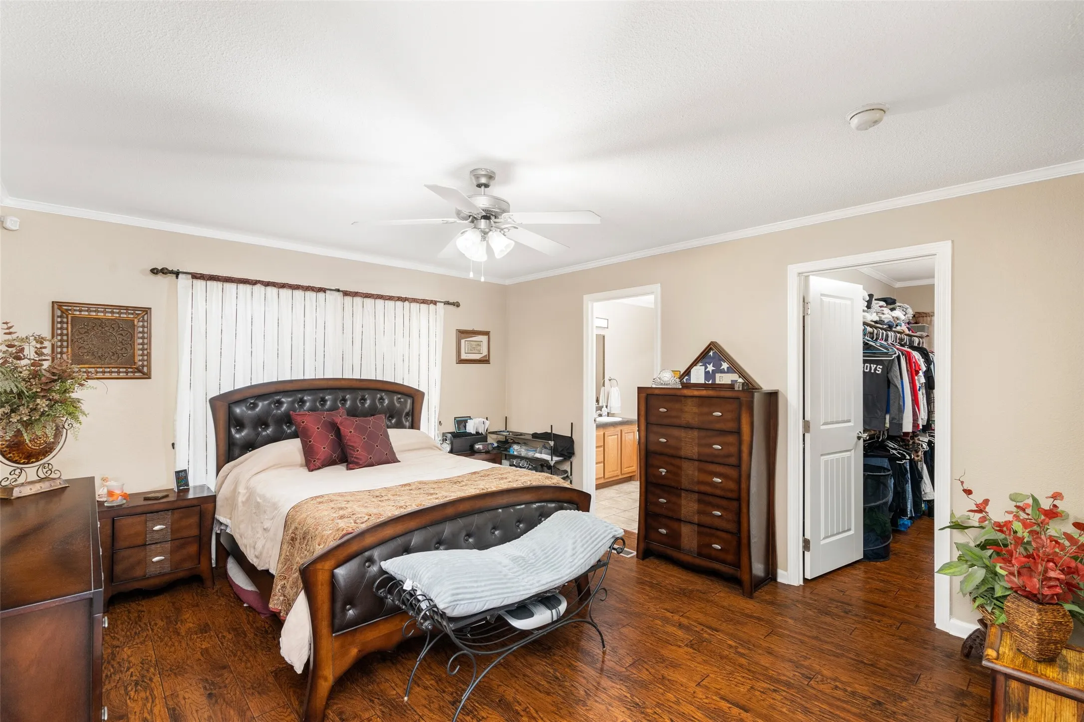Bedroom with ornamental molding, dark wood finished floors, a walk in closet, a ceiling fan, and ensuite bath