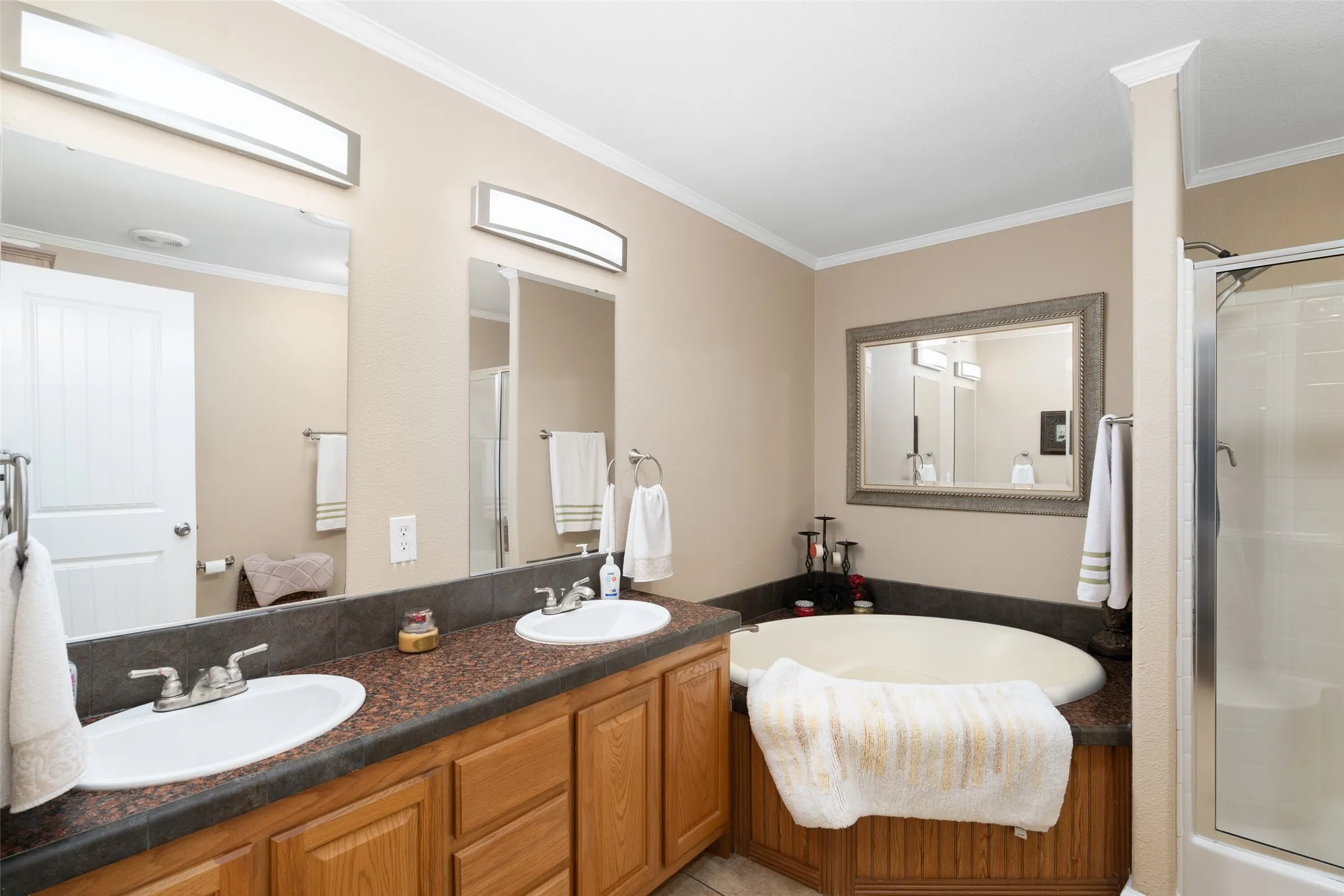 Full bathroom with a shower stall, ornamental molding, a bath, double vanity, and light tile patterned floors