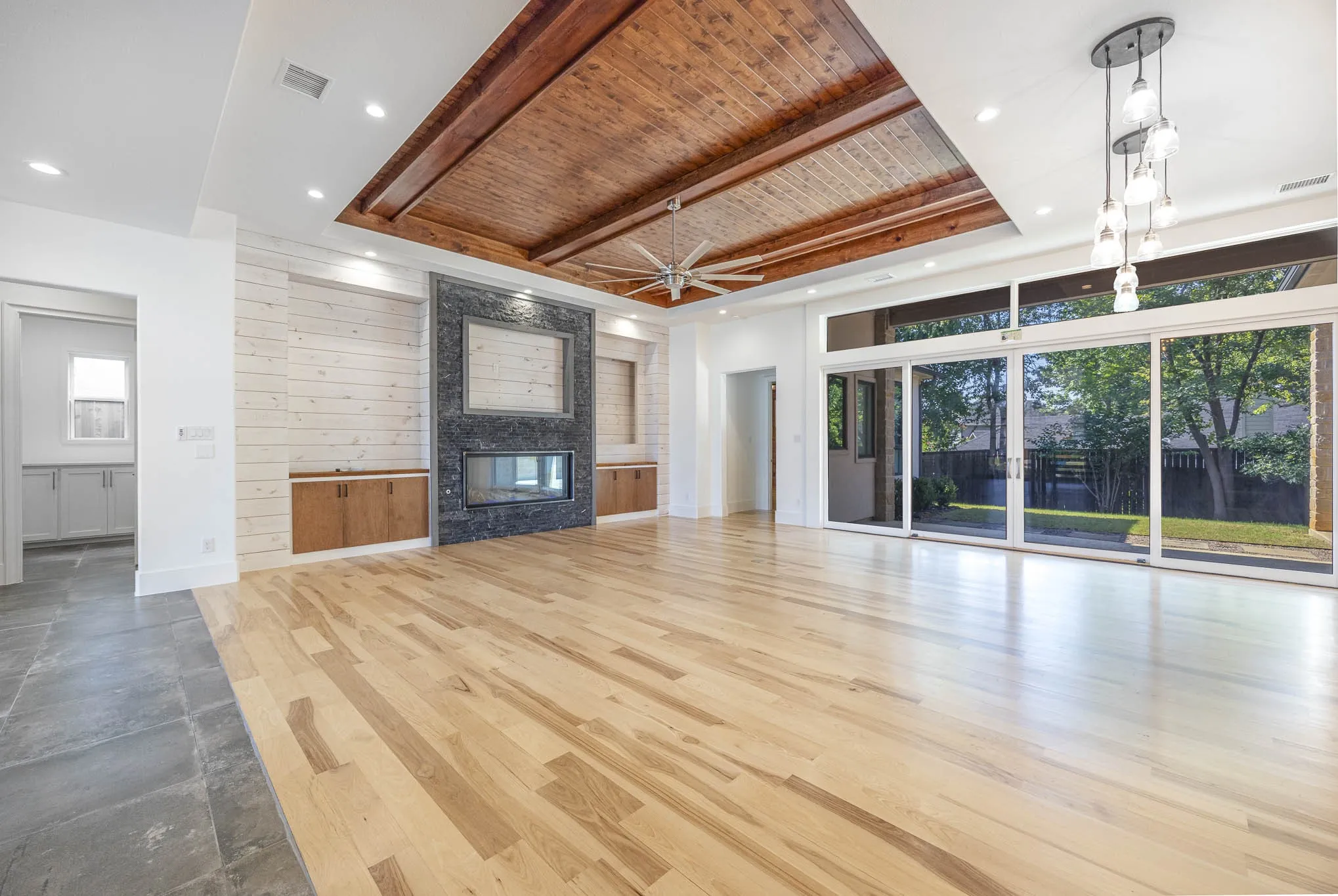 Unfurnished living room with a large fireplace, wood finished floors, wood walls, a raised ceiling, and a wood ceiling with exposed beams