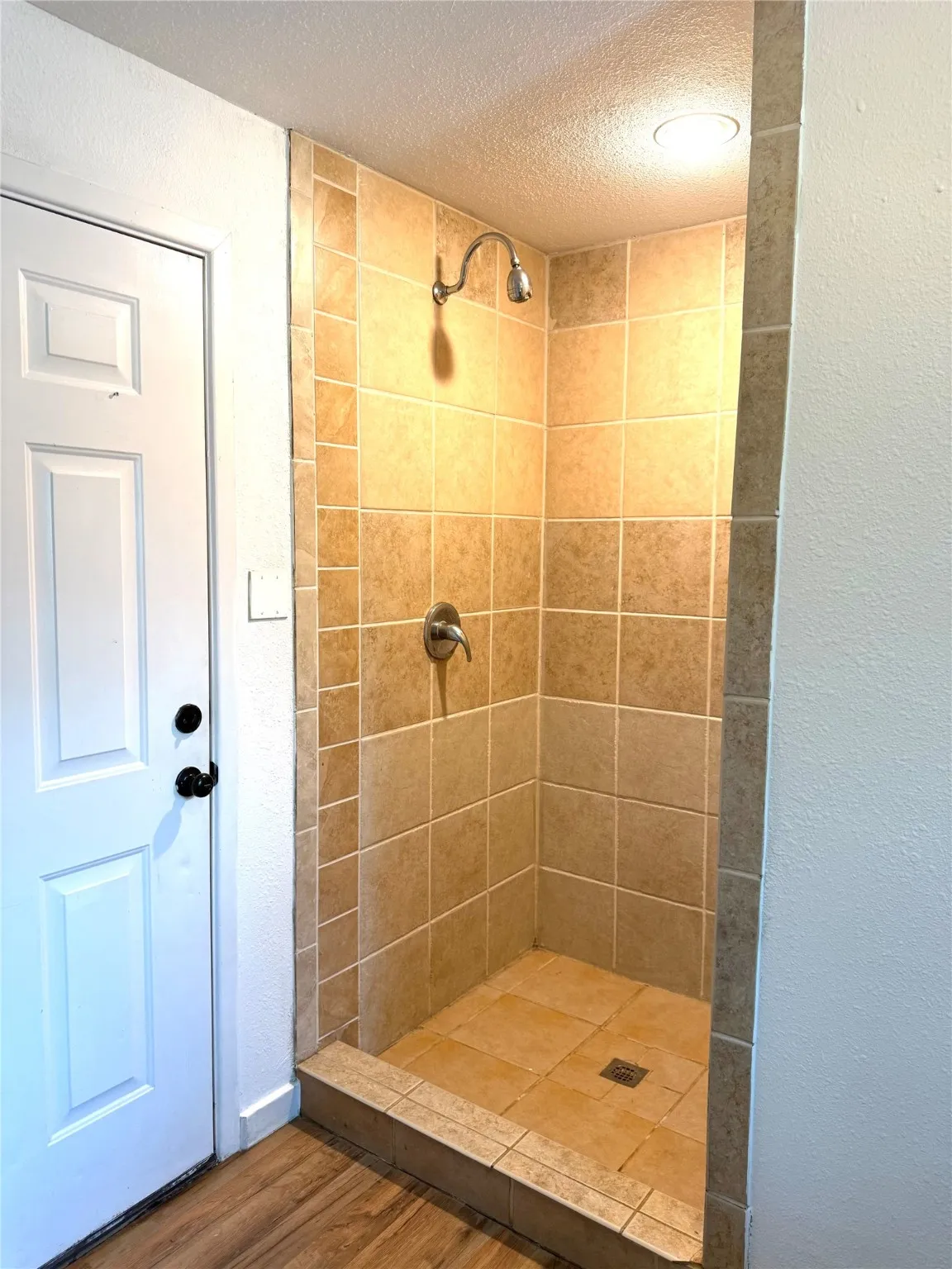 Bathroom with a shower stall, a textured ceiling, a textured wall, and wood finished floors