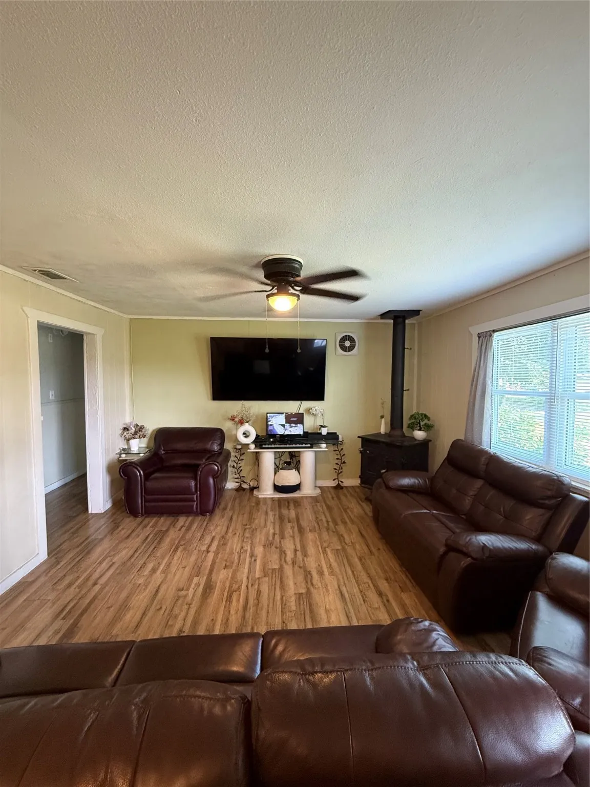 Living area featuring a wood stove, wood finished floors, a textured ceiling, and a ceiling fan