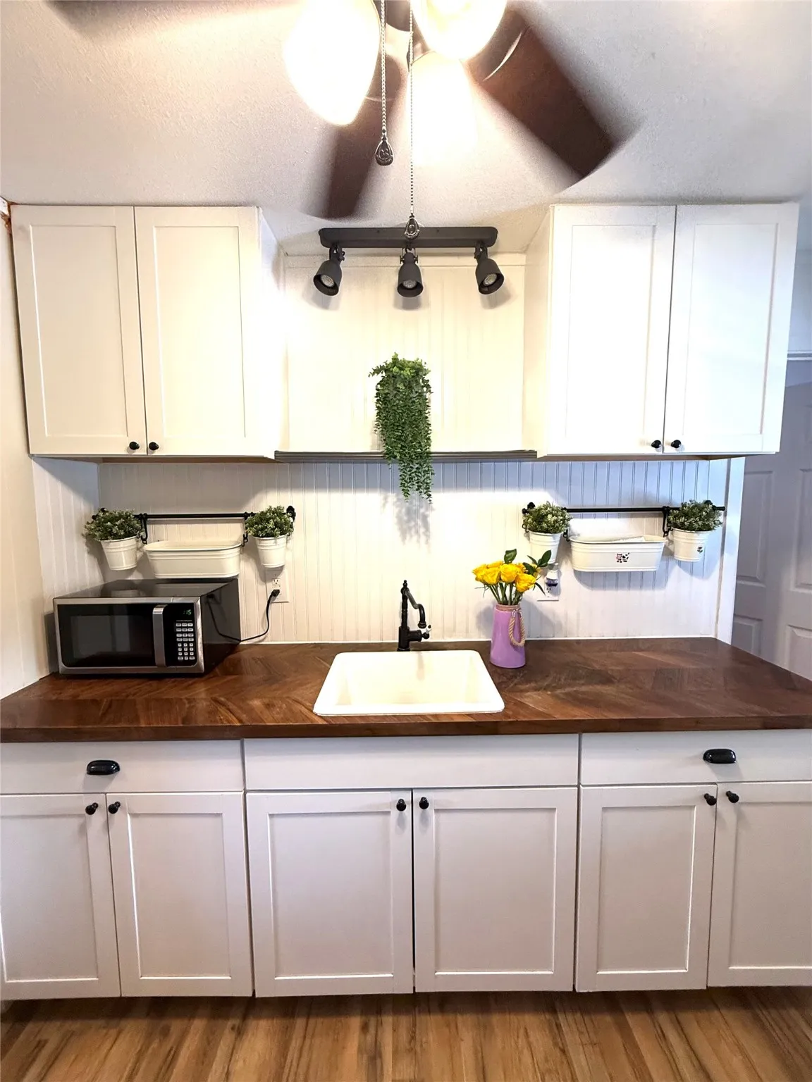 Kitchen with a textured ceiling, butcher block countertops, white cabinets, stainless steel microwave, and light wood-style floors
