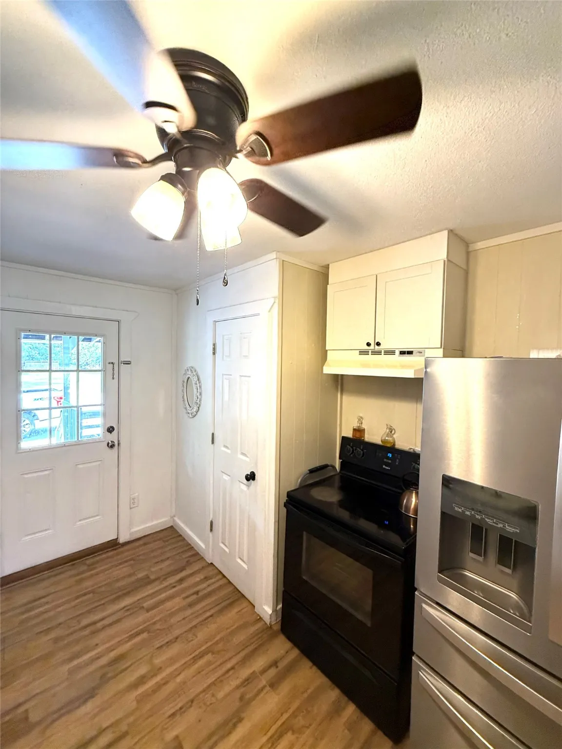 Kitchen featuring stainless steel refrigerator with ice dispenser, black / electric stove, light wood-type flooring, ceiling fan, and a textured ceiling