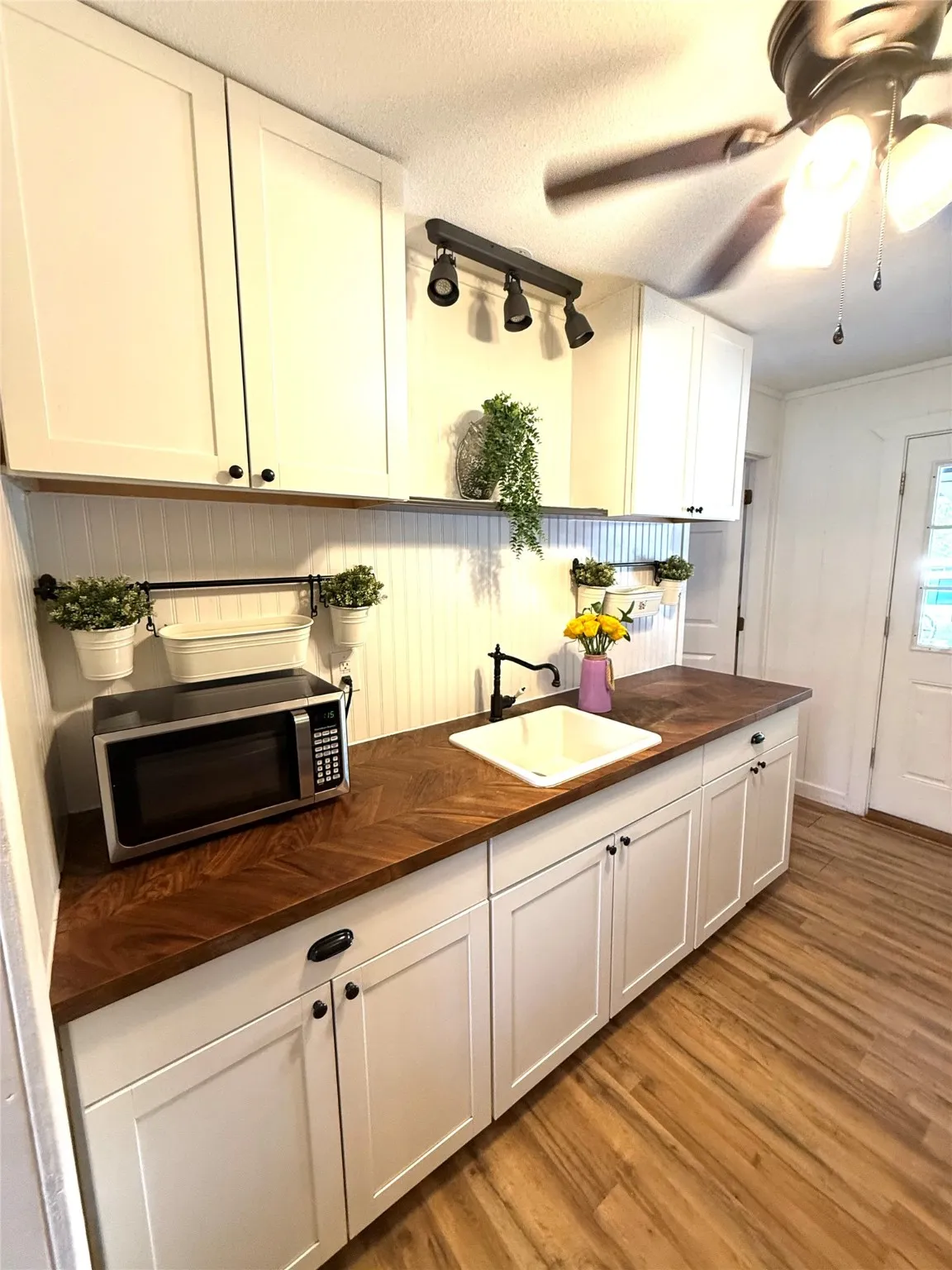 Kitchen with light wood-style flooring, white cabinets, wooden counters, stainless steel microwave, and a textured ceiling