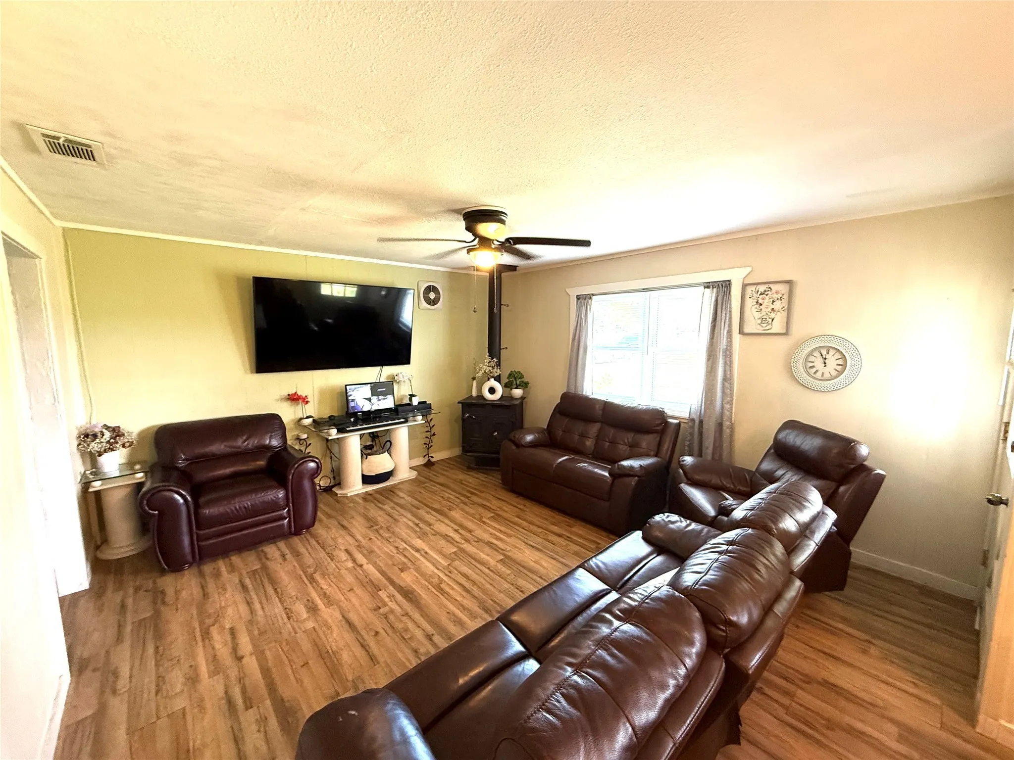 Living area featuring wood finished floors, ceiling fan, ornamental molding, and a textured ceiling