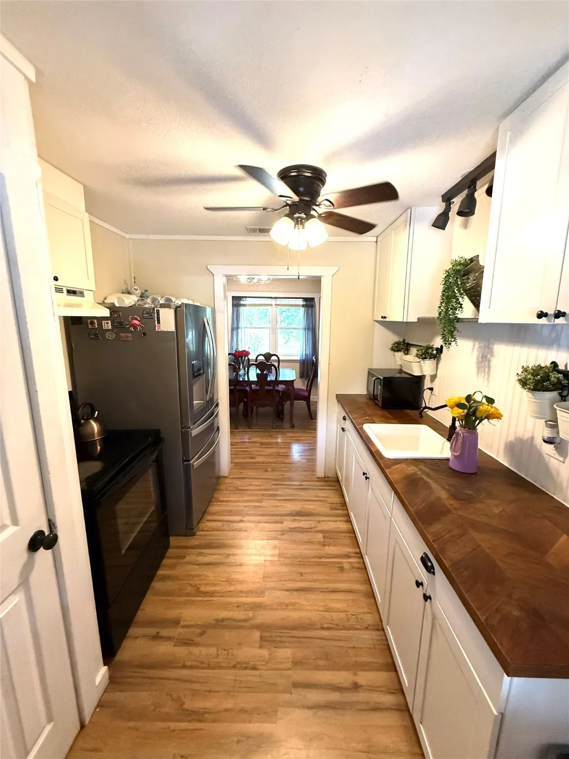 Kitchen with white cabinets, a ceiling fan, light wood-type flooring, black appliances, and under cabinet range hood