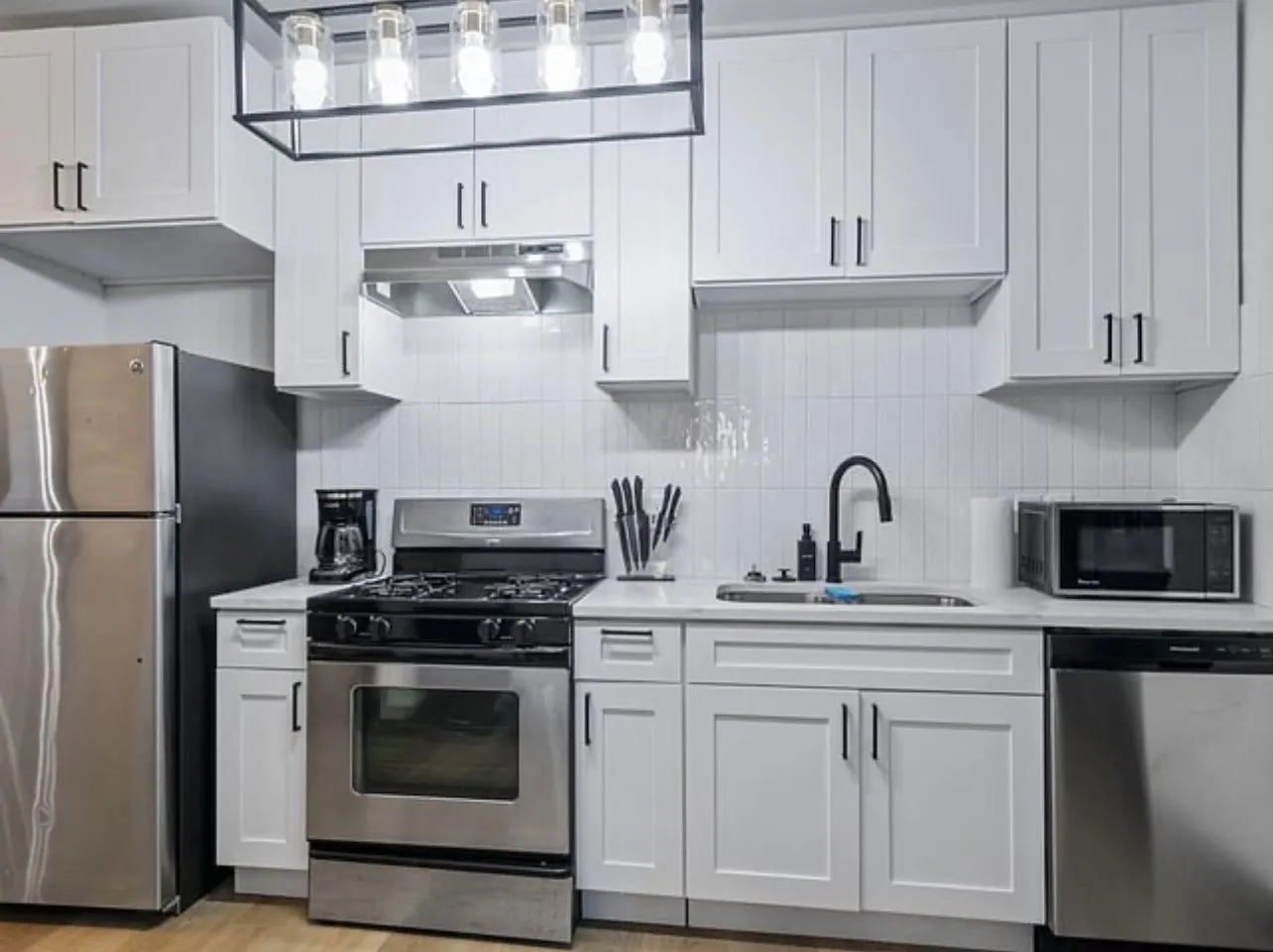Kitchen with white cabinets, appliances with stainless steel finishes, under cabinet range hood, and backsplash