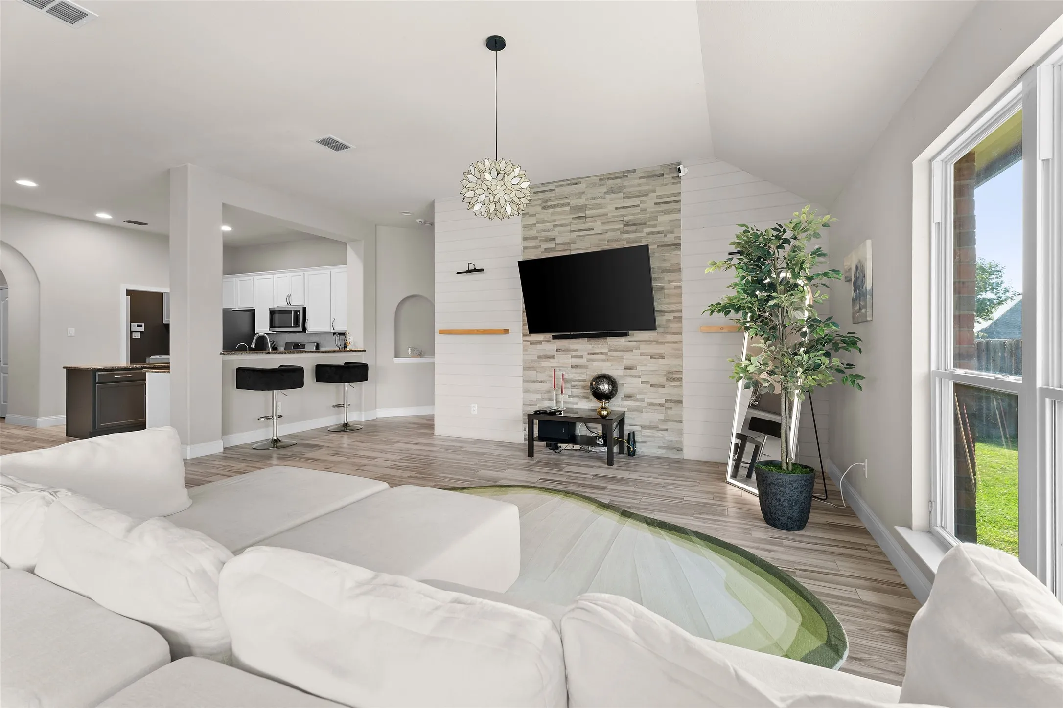 Living room featuring light wood-style flooring, an accent wall, a chandelier, arched walkways, and lofted ceiling