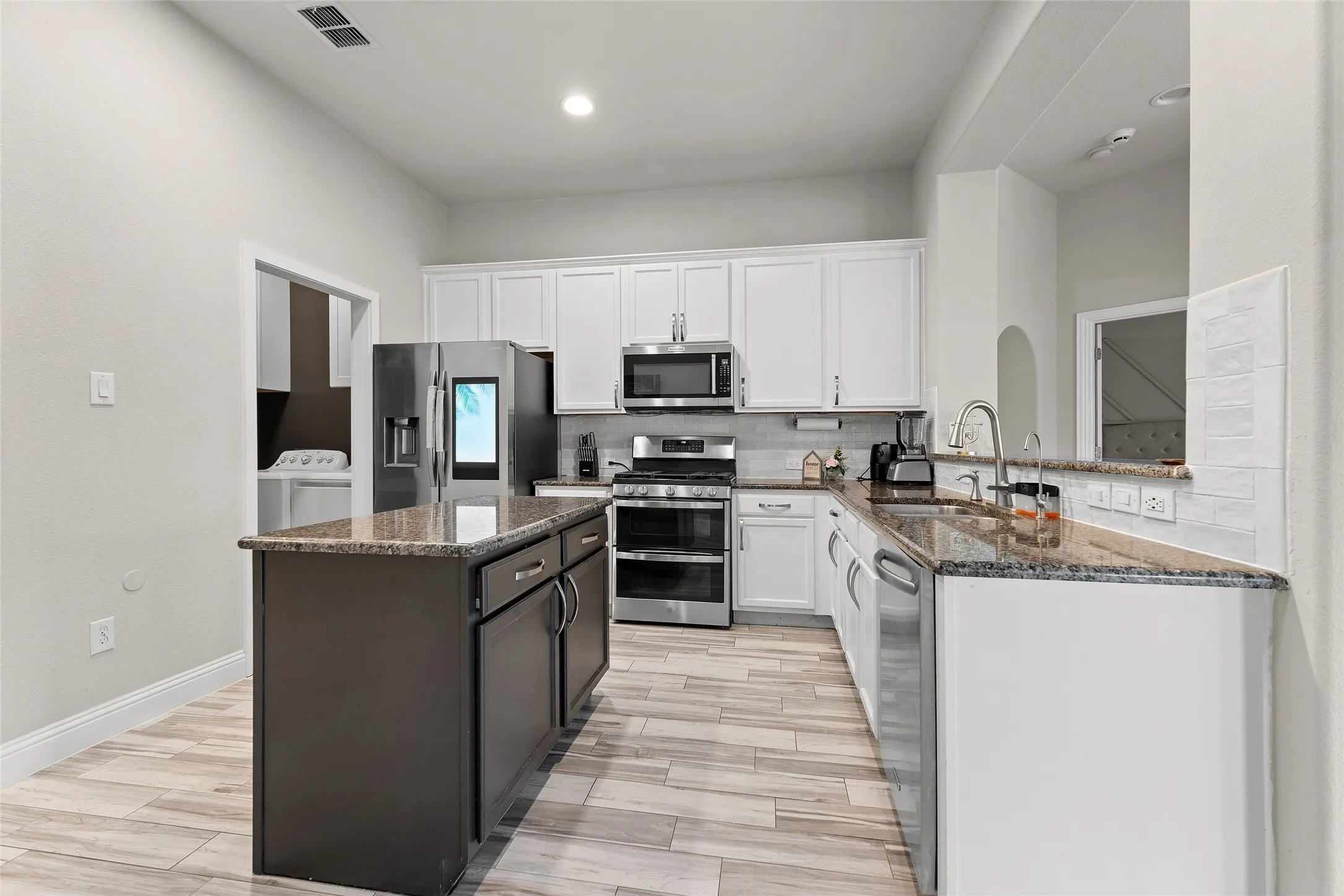 Kitchen with backsplash, dark stone countertops, appliances with stainless steel finishes, white cabinets, and recessed lighting