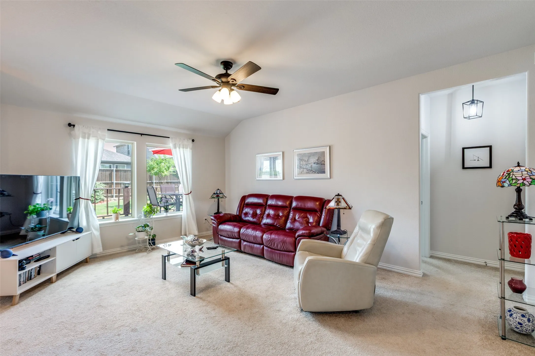 Carpeted living room with a ceiling fan and vaulted ceiling