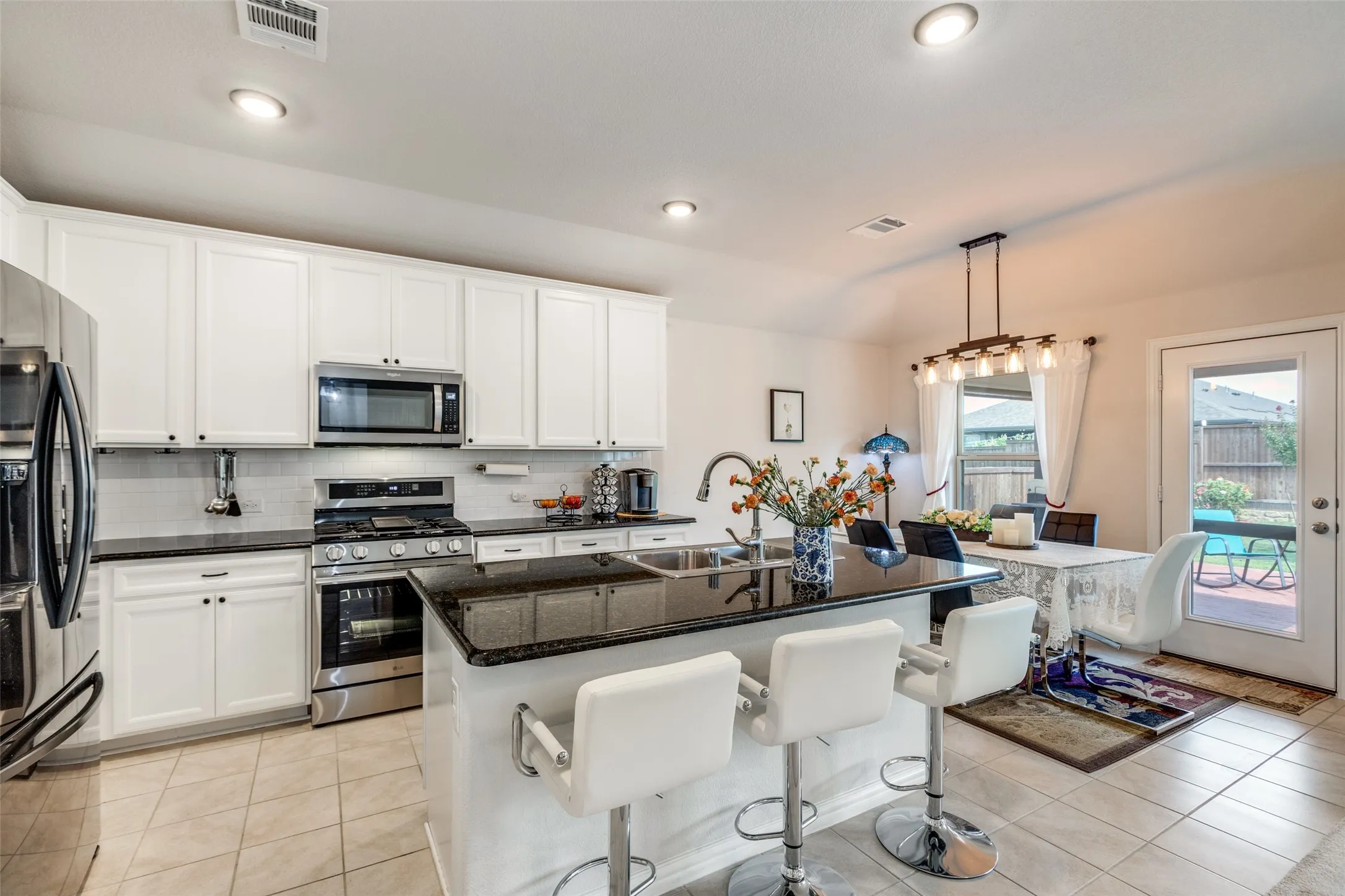Kitchen with tasteful backsplash, stainless steel appliances, light tile patterned floors, white cabinets, and a center island with sink