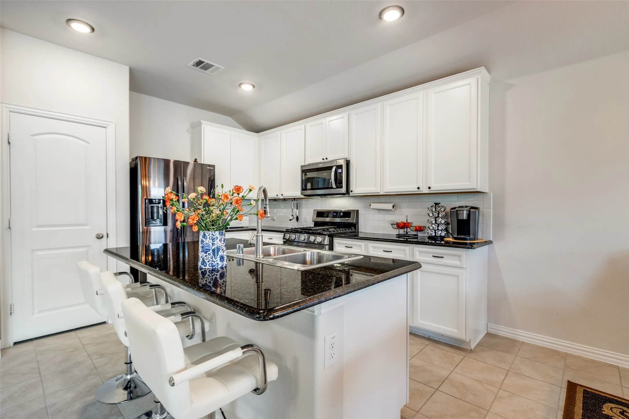 Kitchen with a kitchen breakfast bar, dark stone countertops, decorative backsplash, white cabinetry, and a kitchen island with sink