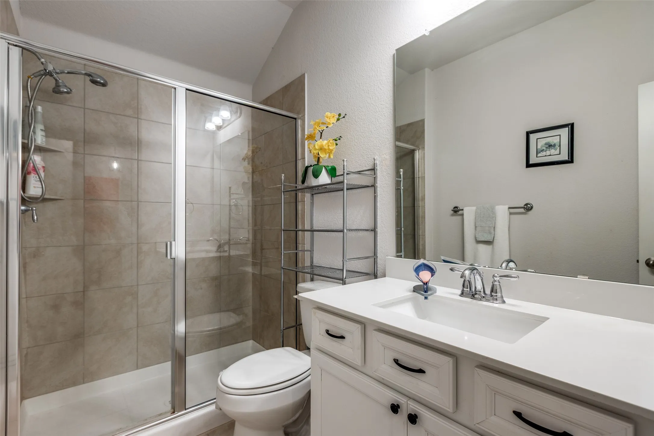 Bathroom with a shower stall, vanity, a textured wall, and lofted ceiling